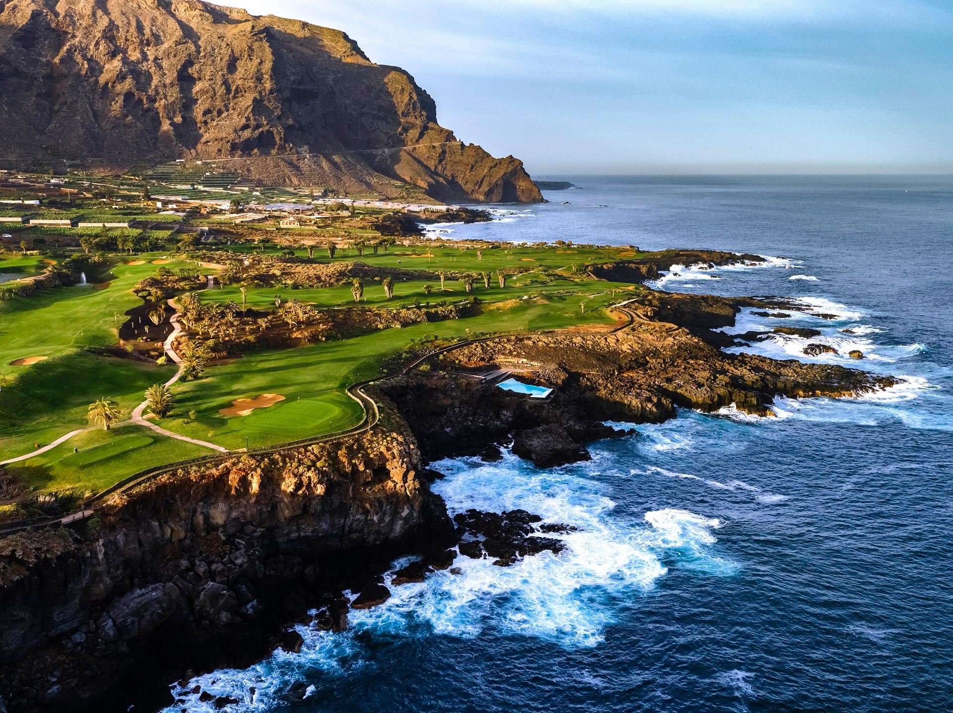 Overhead view of a coastal fairway with mountains towering over