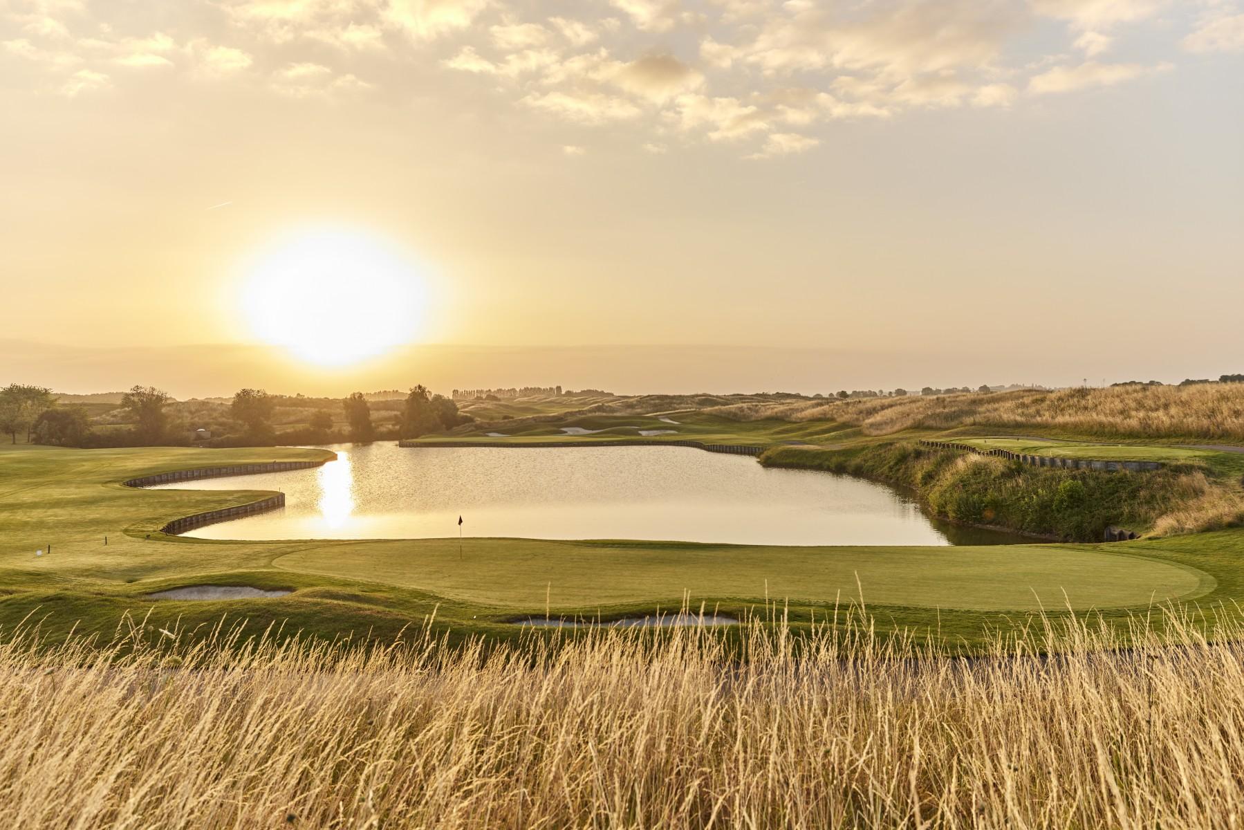 Sun shining over a smooth green next to a water hazard