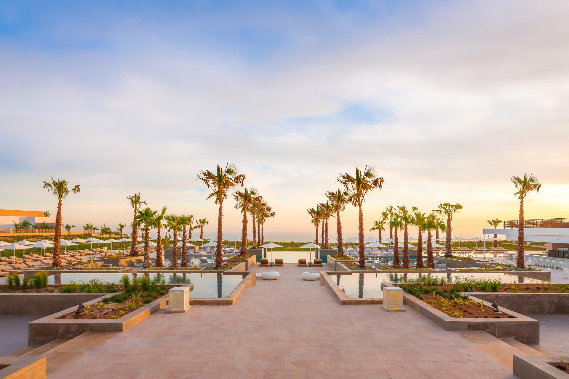 A palm tree lined walkway separating the pools at Hyatt Place Taghazout Bay