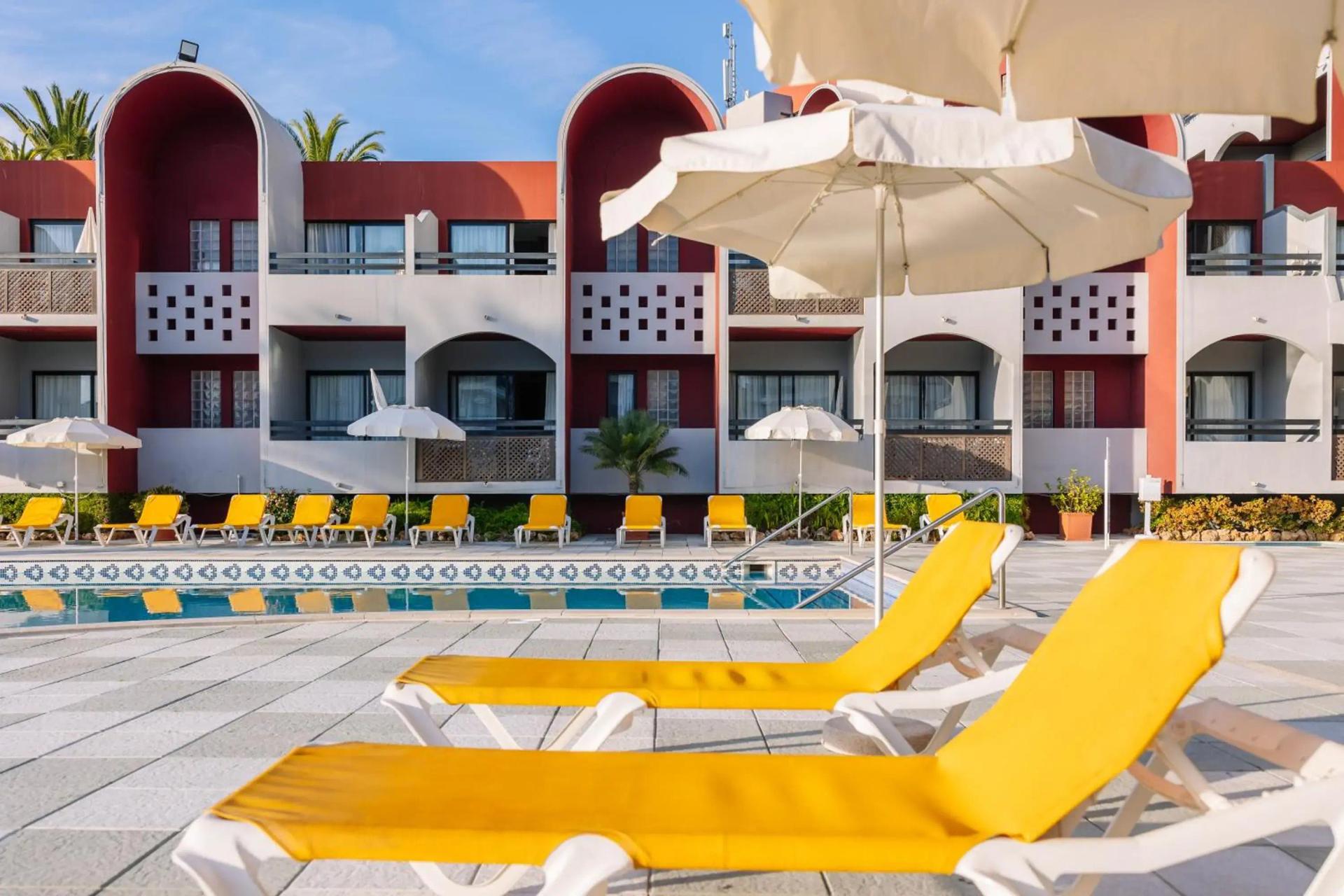 Outdoor swimming pool lined with sunbeds at Muthu Oura Praia Hotel